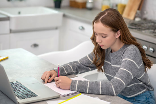 Girl sitting at a table with laptop doing schoolwork